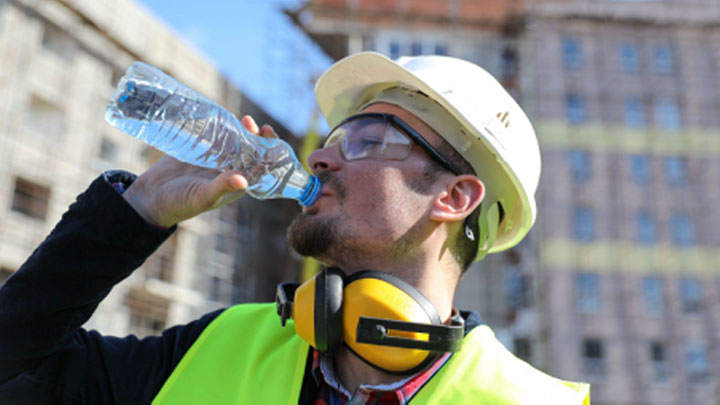 A construction worker drinking fluids to stay hydrated on a hot summer day