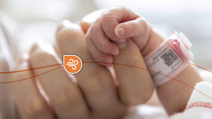 Close up of a newborn baby's hand wrapped around a grownup's finger while wearing a hospital band.