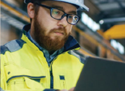 A bearded man wearing a safety vest and a hard hat using a computer.